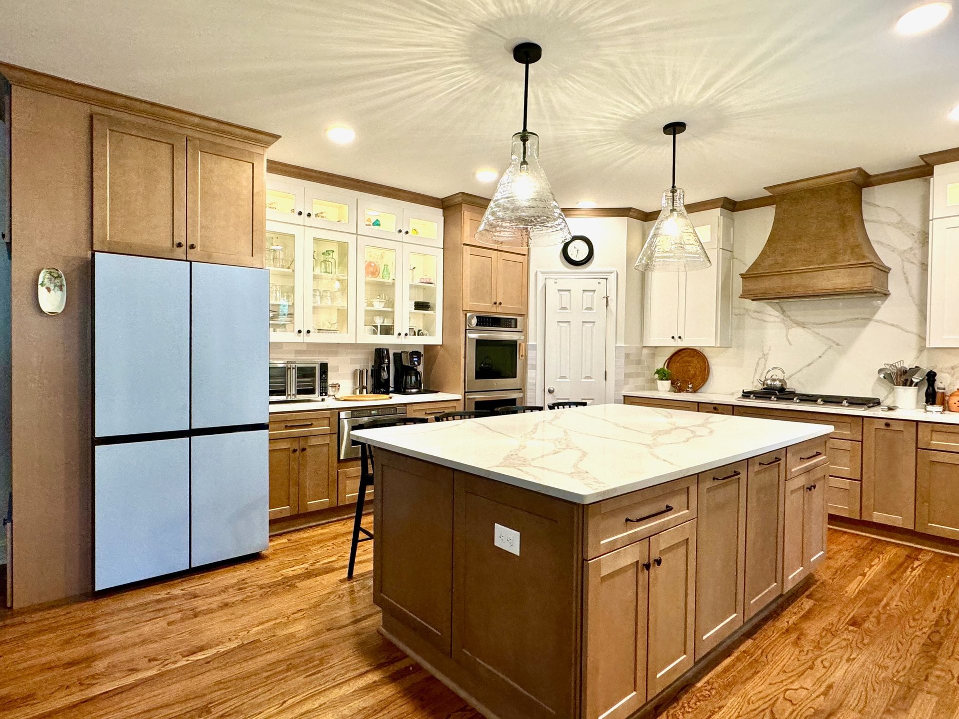 Bright kitchen with blue refrigerator, wood cabinets, central island, and white range hood