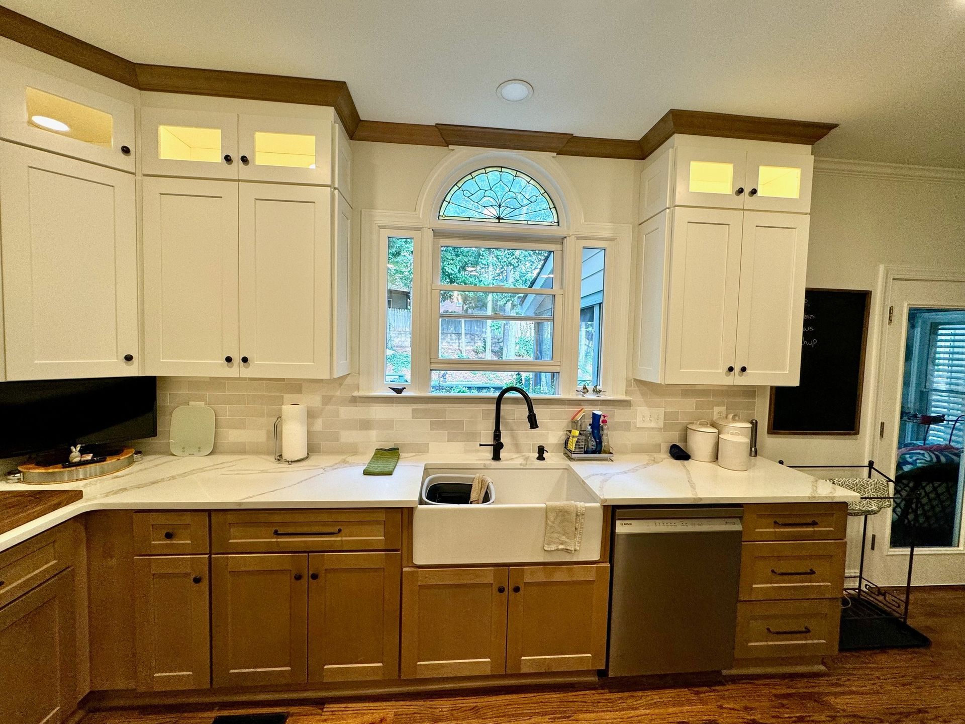 Bright kitchen with white cabinets, farmhouse sink, and arched window above the counter.
