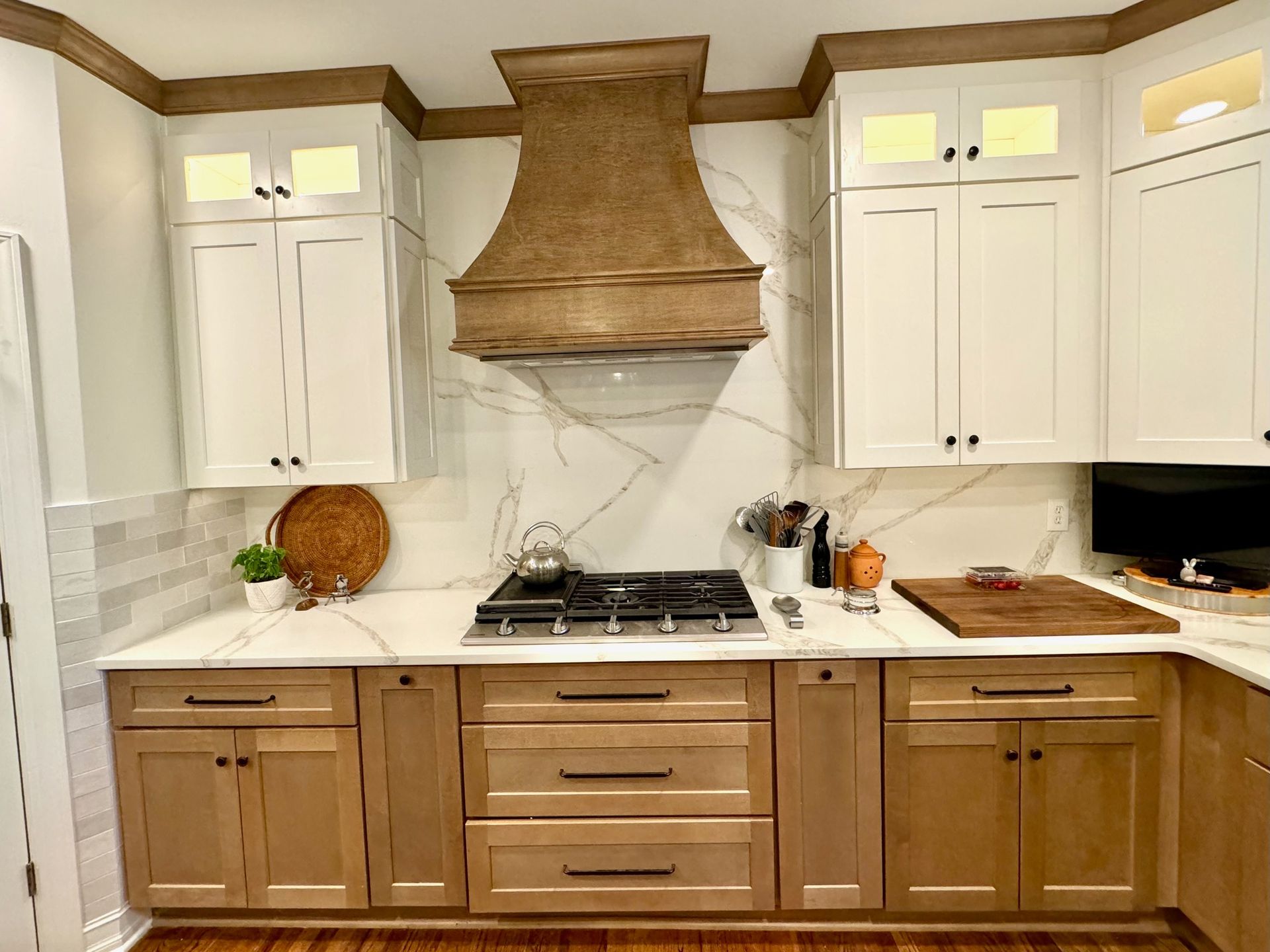 Modern kitchen with white cabinets, wood lower cabinets, marble backsplash, and a gas cooktop under a decorative hood