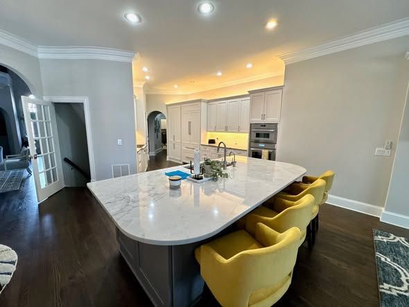 Modern kitchen with a large white island, yellow stools, stainless appliances, and dark hardwood floors