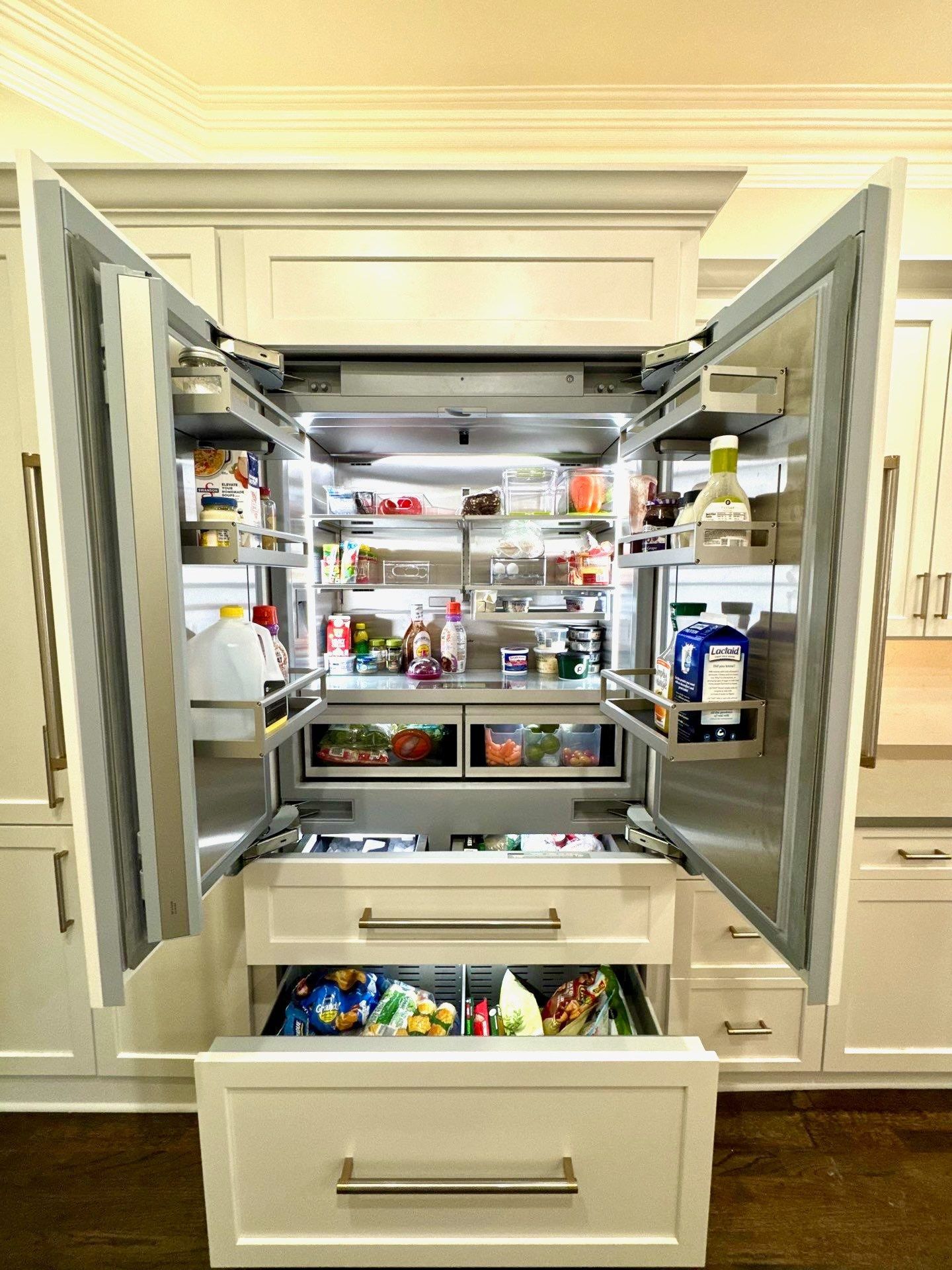 Open refrigerator with organized shelves and a pulled-out crisper drawer in a bright kitchen