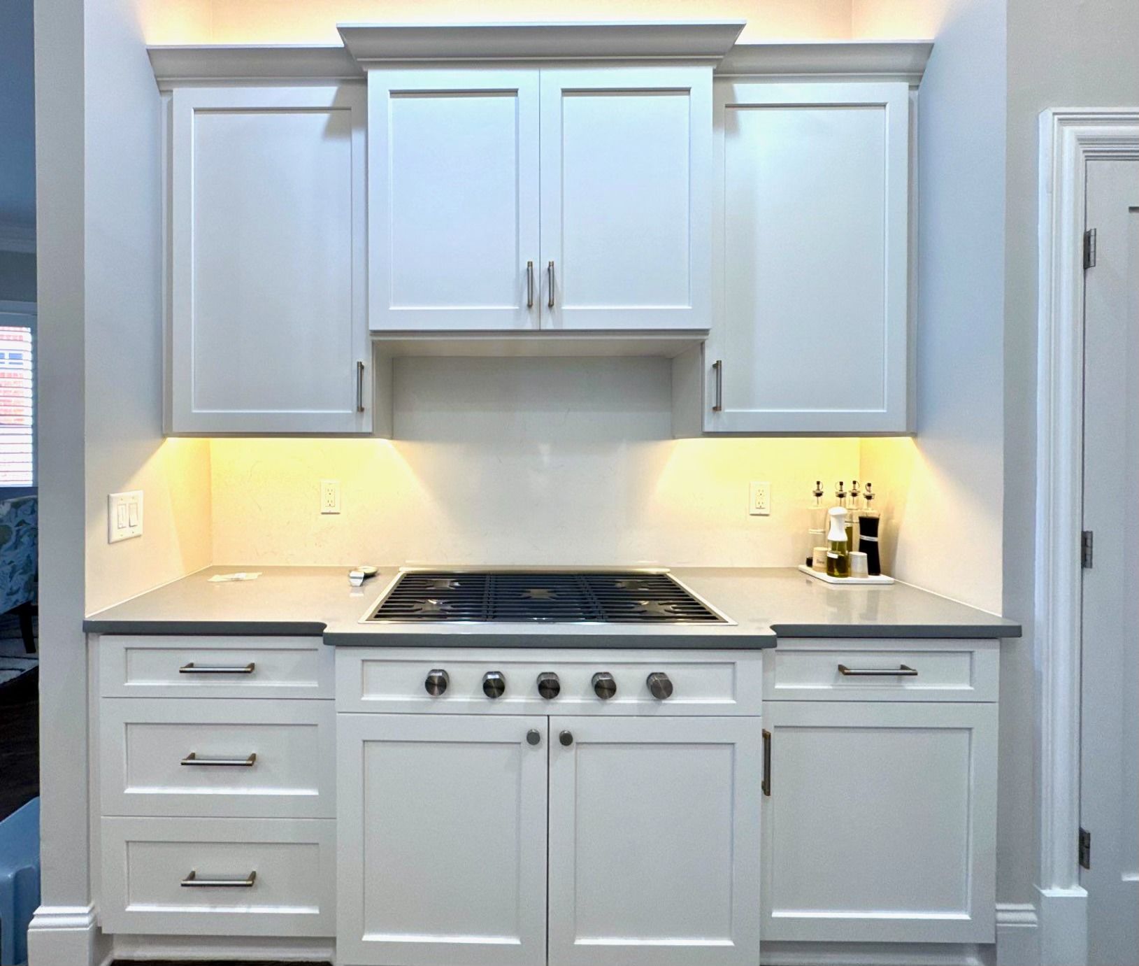 Modern white kitchen with gray countertops, stainless stove, and under-cabinet lighting