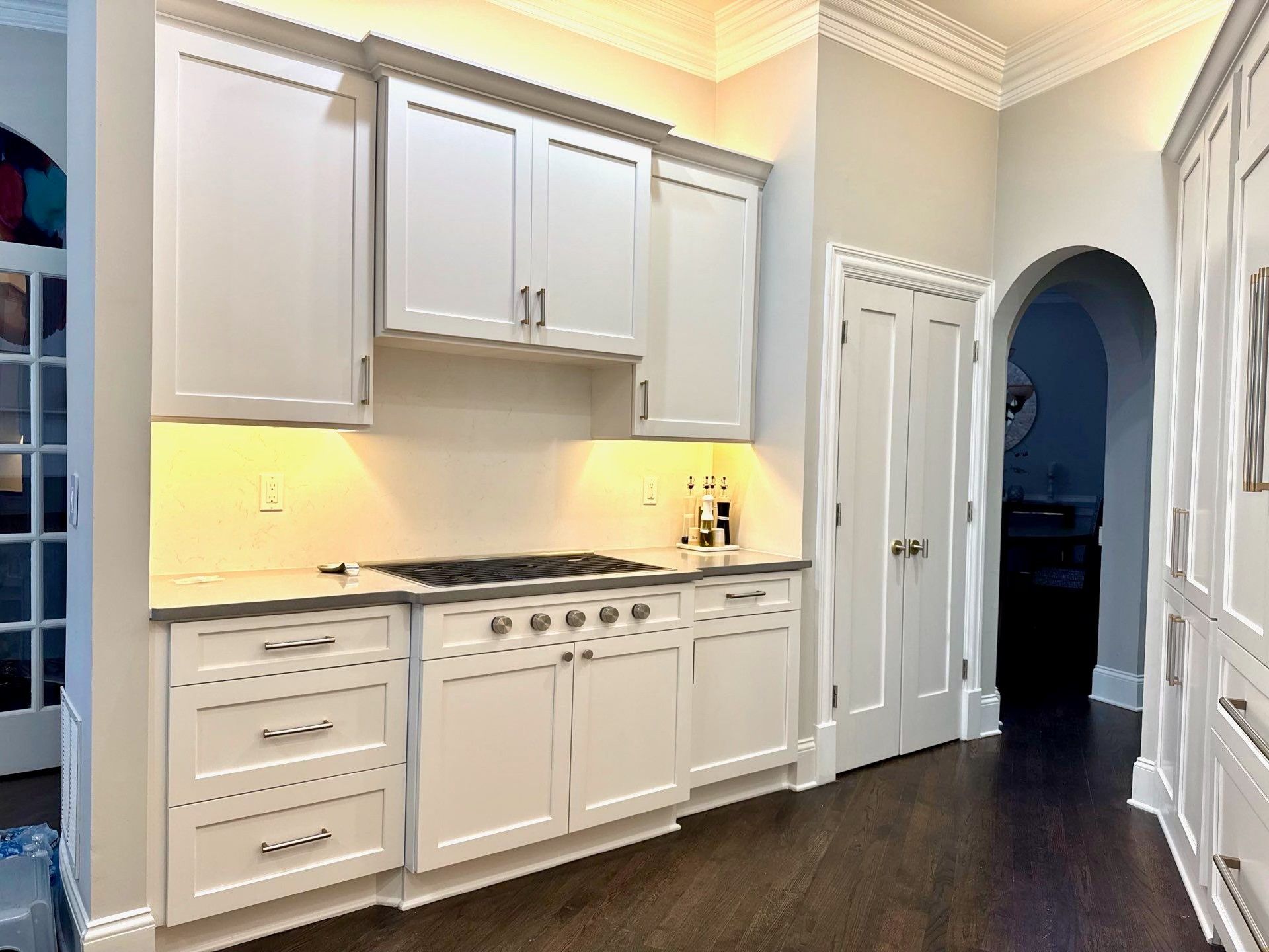 Bright white kitchen with cabinets, dark wood floors, and arched doorway.