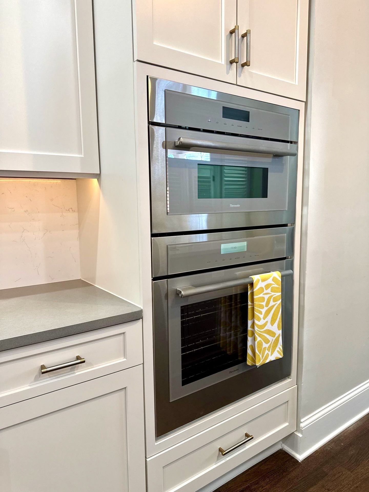Built-in stainless steel double oven in a white kitchen, with a yellow towel on the lower handle