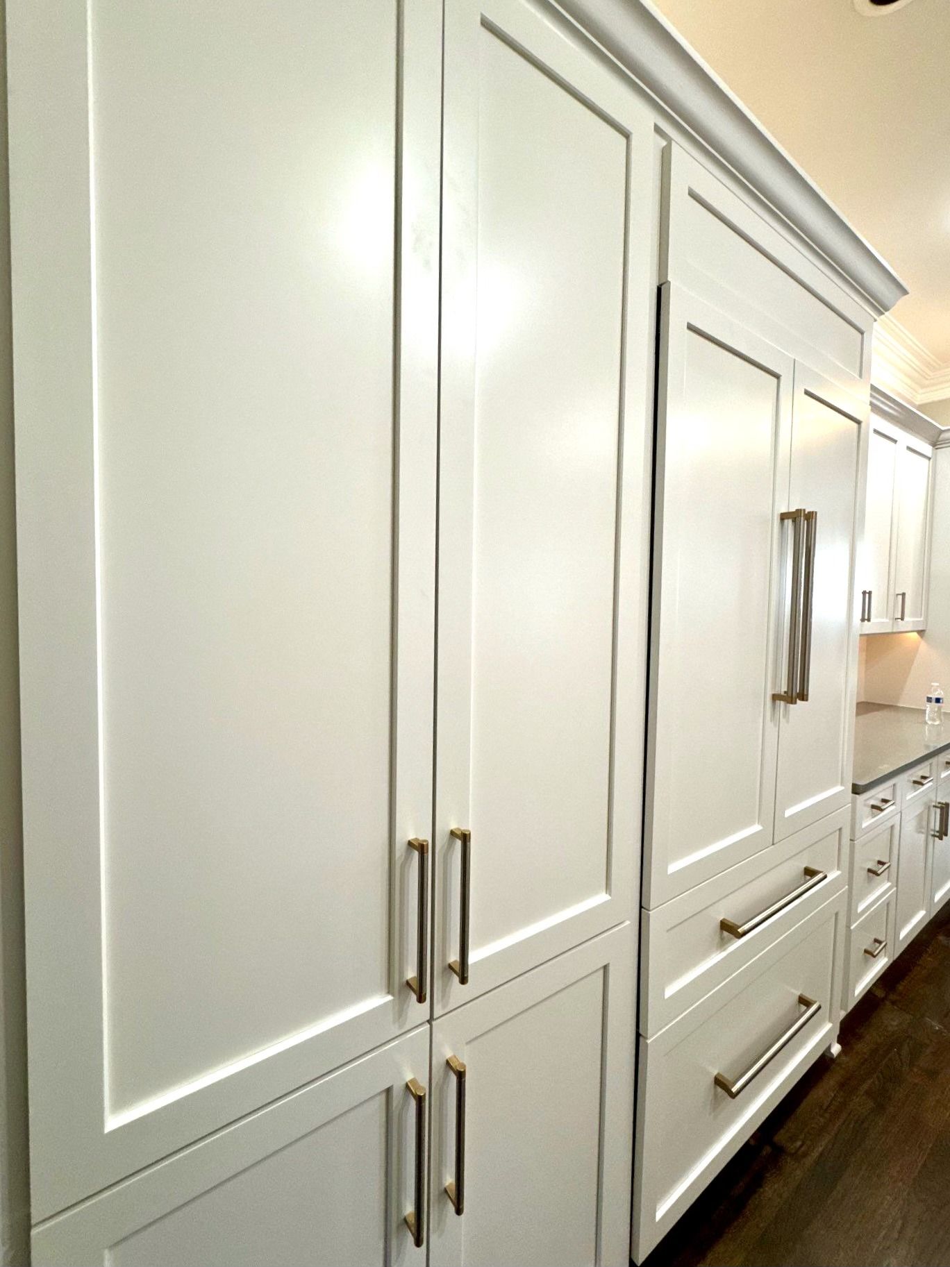 White built-in kitchen cabinets with brass handles lining a narrow hallway.