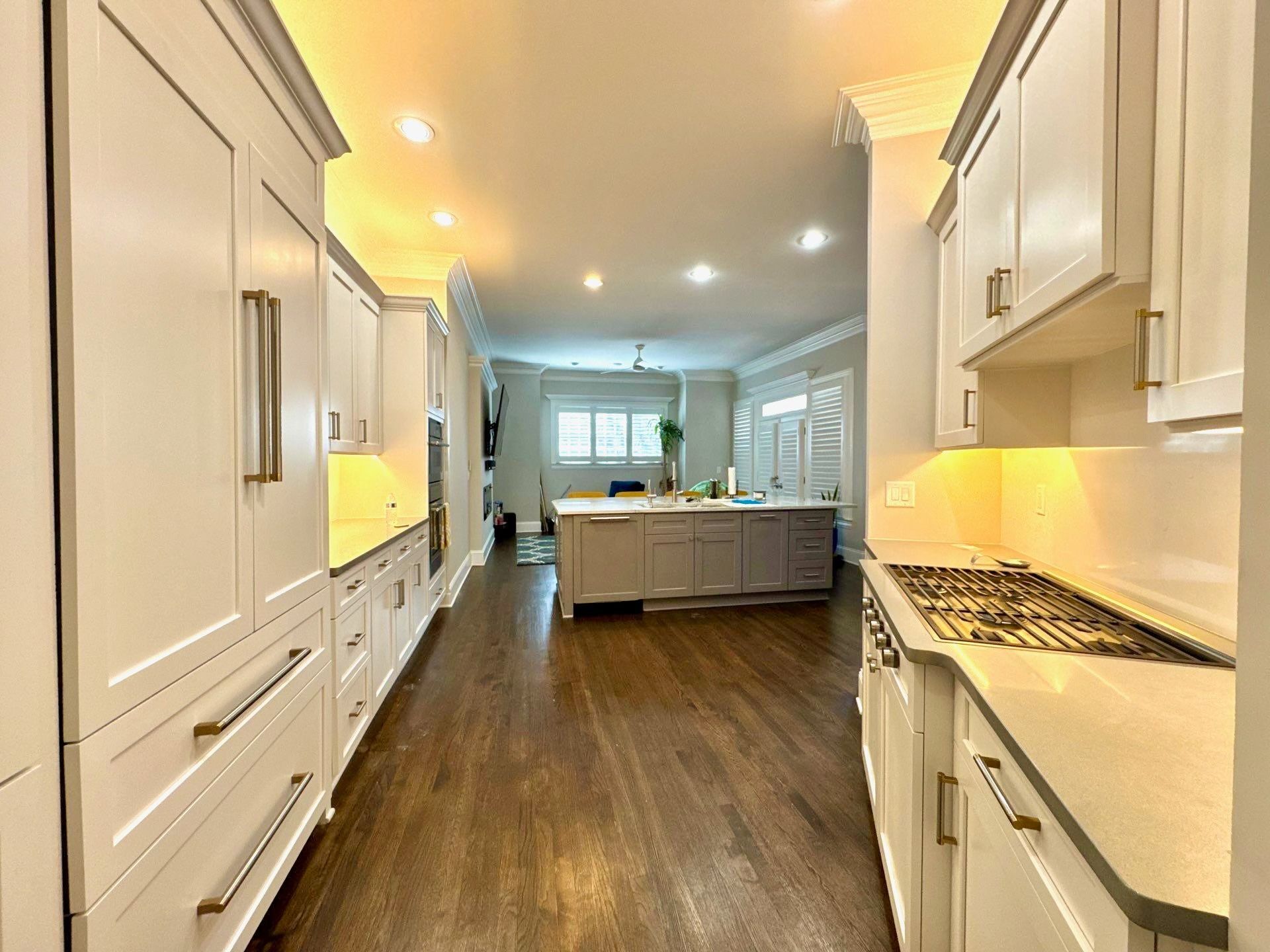 Bright modern kitchen with white cabinets, dark wood floor, and an island leading to a windowed dining area
