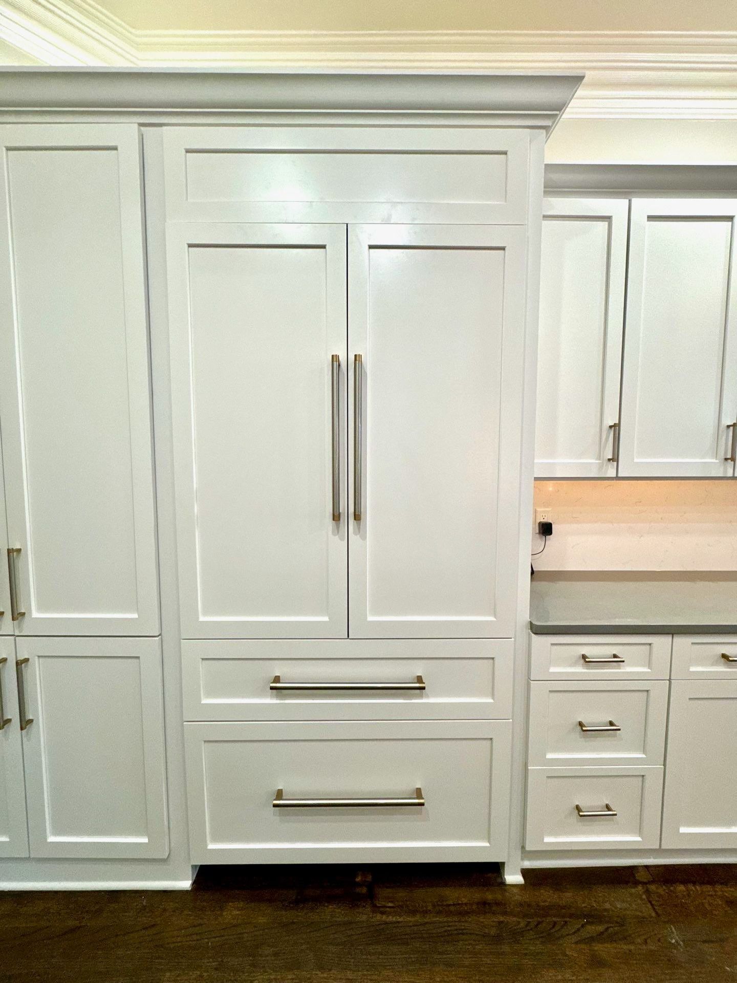 White built-in kitchen cabinetry with a large refrigerator and drawers in a bright kitchen.