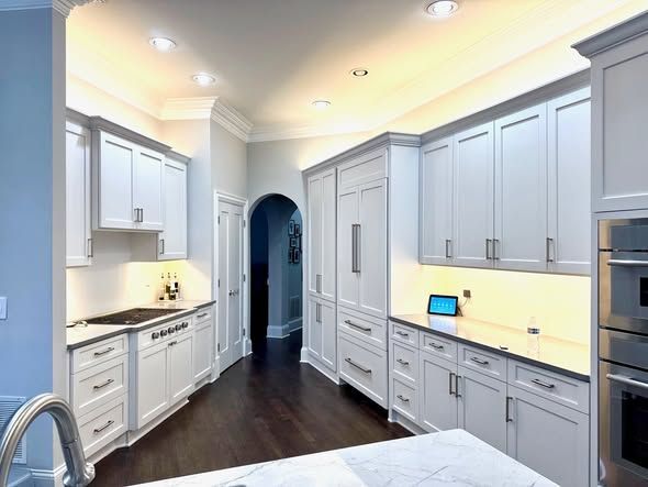 Bright white kitchen with long cabinets, dark wood floor, and a stainless refrigerator.