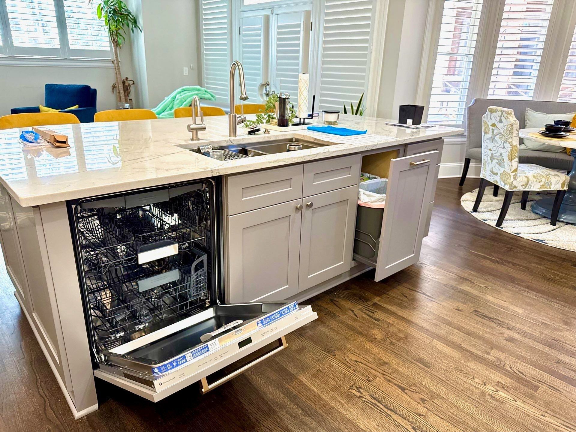 Modern kitchen island with open dishwasher, sink, and wood flooring in a bright home interior