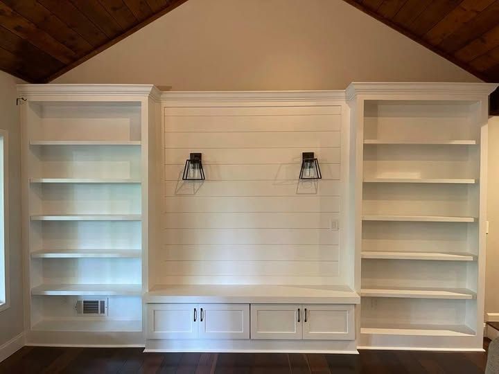 Built-in white shelving and cabinets centered on a paneled wall beneath a vaulted wood ceiling.