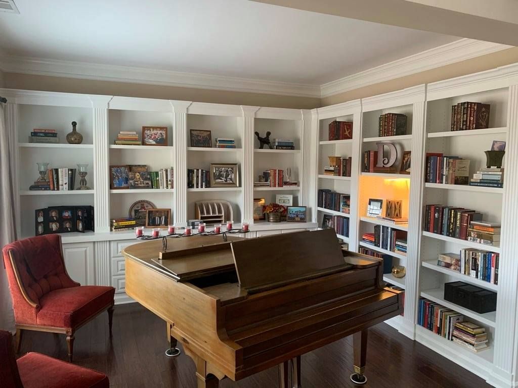 Living room with a grand piano, red chair, and white bookshelves filled with books and decor