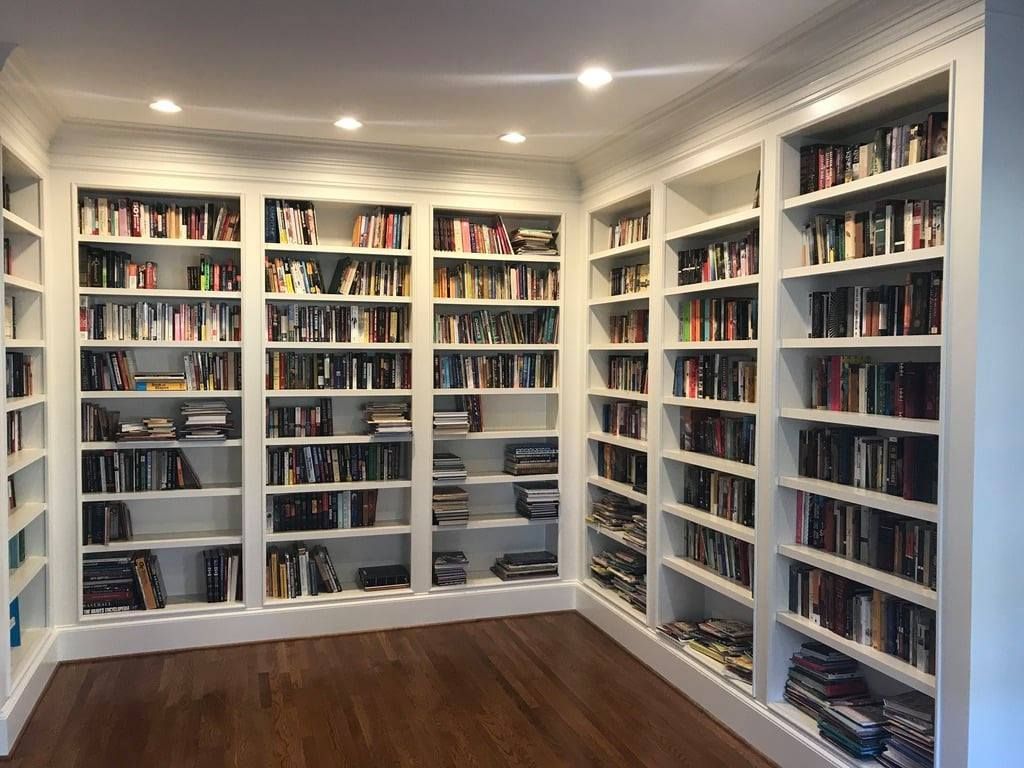 Bright empty library room with white built-in bookshelves filled with books and wood floors