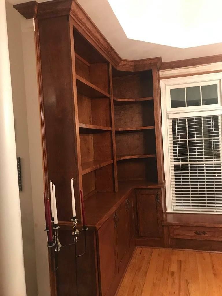 Built-in dark wood bookshelves in a corner beside a window with white blinds and hardwood floors