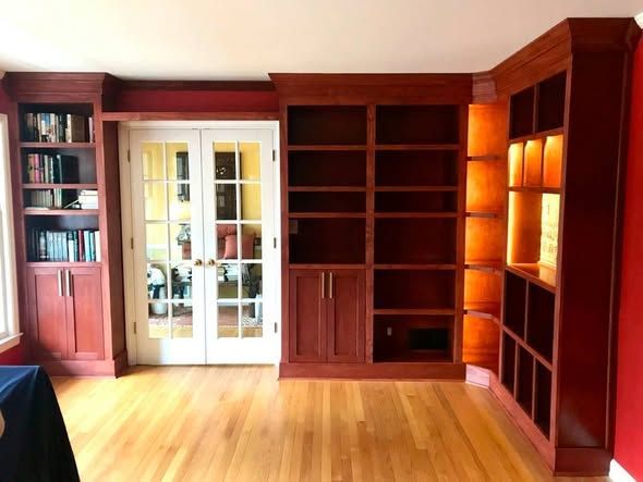 Red-walled built-in bookshelf room with wood floors and French doors to another room