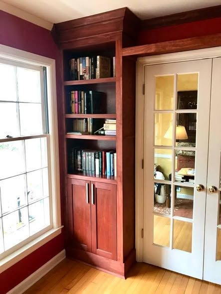 Built-in wooden bookshelf beside white French doors in a pink-walled room