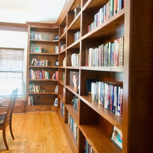 Wood-paneled home library with built-in bookshelves filled with books and a hardwood floor.