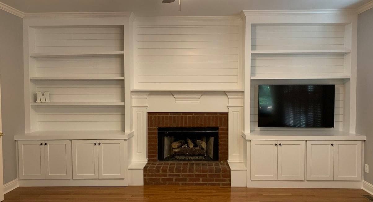 Built-in white living room shelves flanking a fireplace, with a TV on the right and hardwood floors.