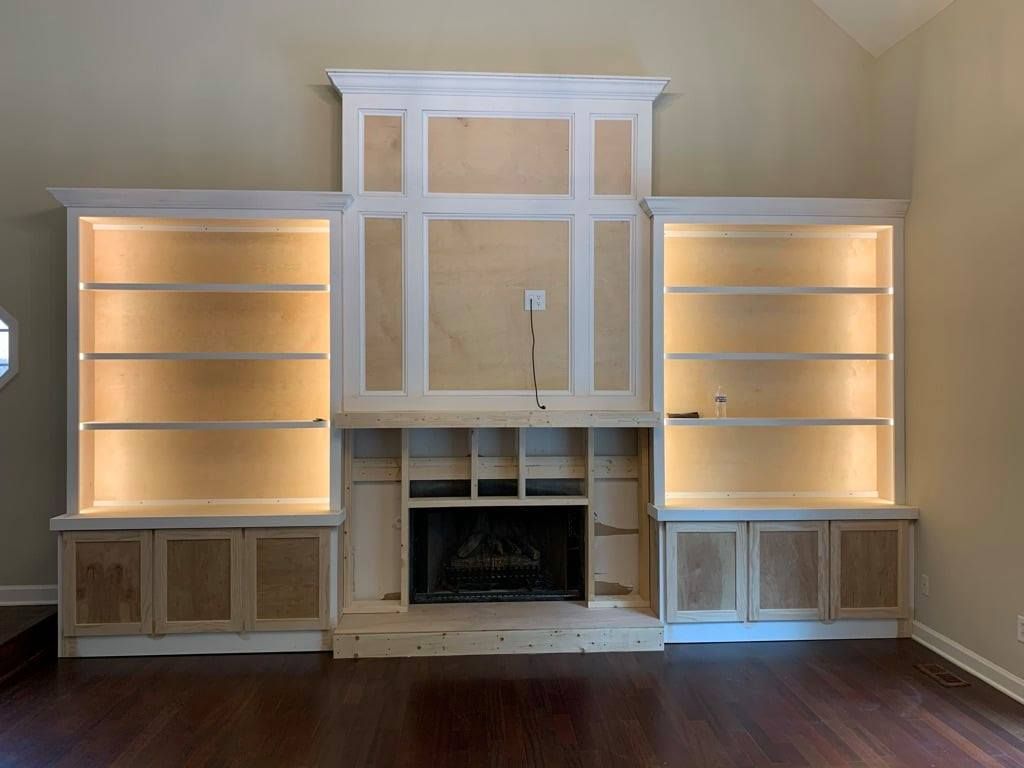 Built-in living room wall unit with lit shelves, cabinets, and a central fireplace opening