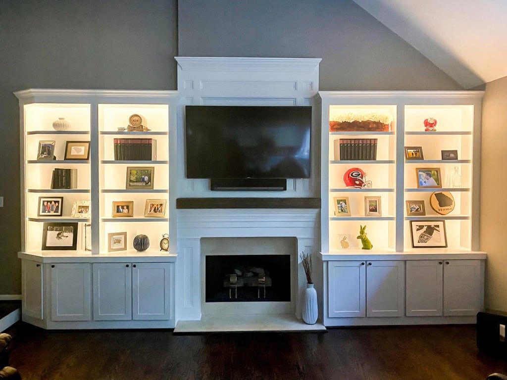 Built-in white entertainment wall with TV, fireplace, and lit display shelves on both sides