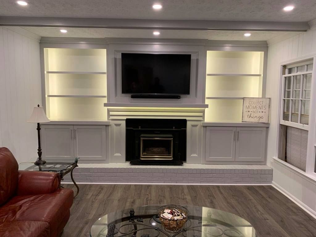 Bright living room with built-in shelves, a mounted TV above the fireplace, and a brown leather sofa in the foreground