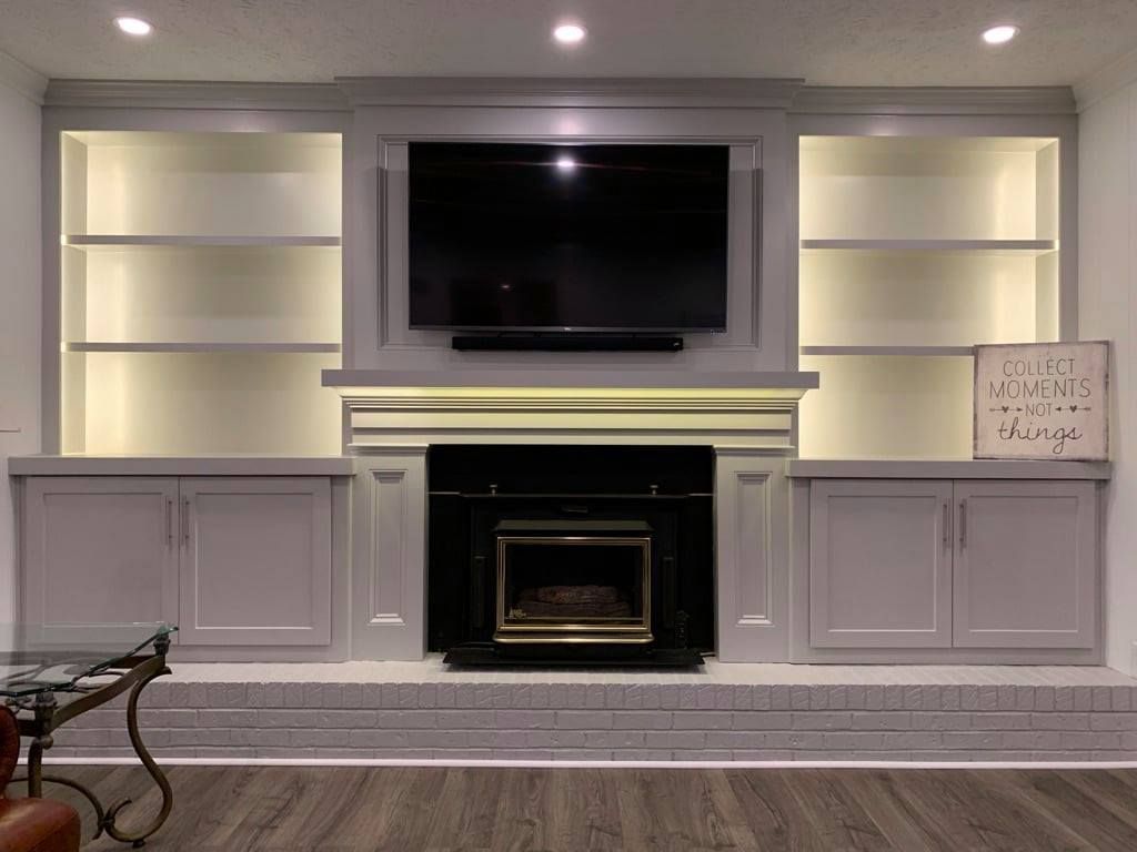 Built-in living room wall with TV, fireplace, and white shelves and cabinets