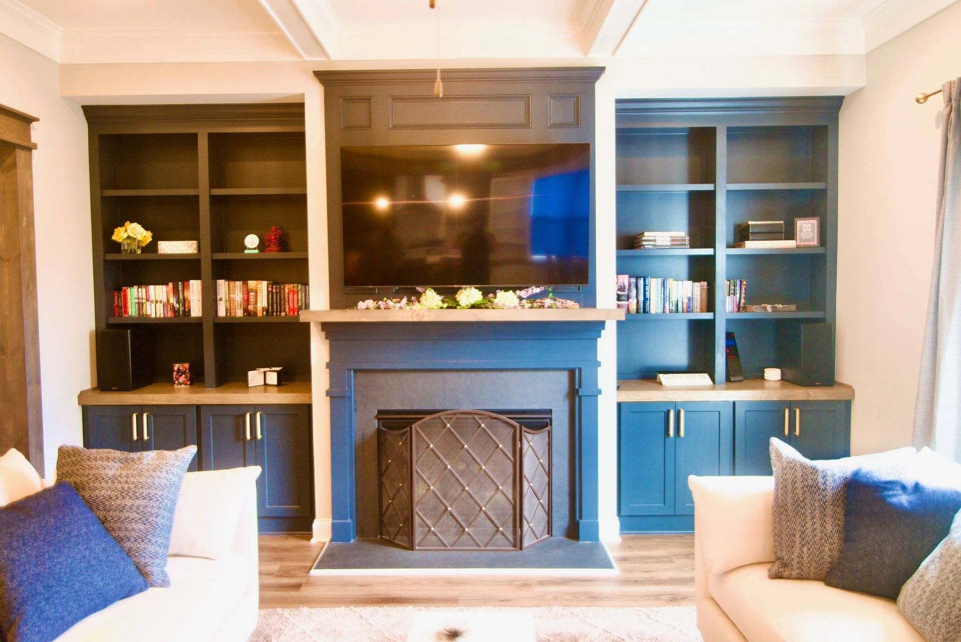 Blue built-in shelves flanking a fireplace with window seat, framed by two beige armchairs in a cozy living room