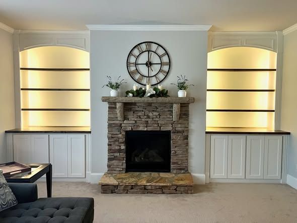 Living room fireplace with stone surround, large wall clock, and lit built-in shelves on both sides