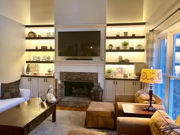 Cozy living room with fireplace, built-in shelves, neutral decor, and a lit table lamp by sliding glass doors