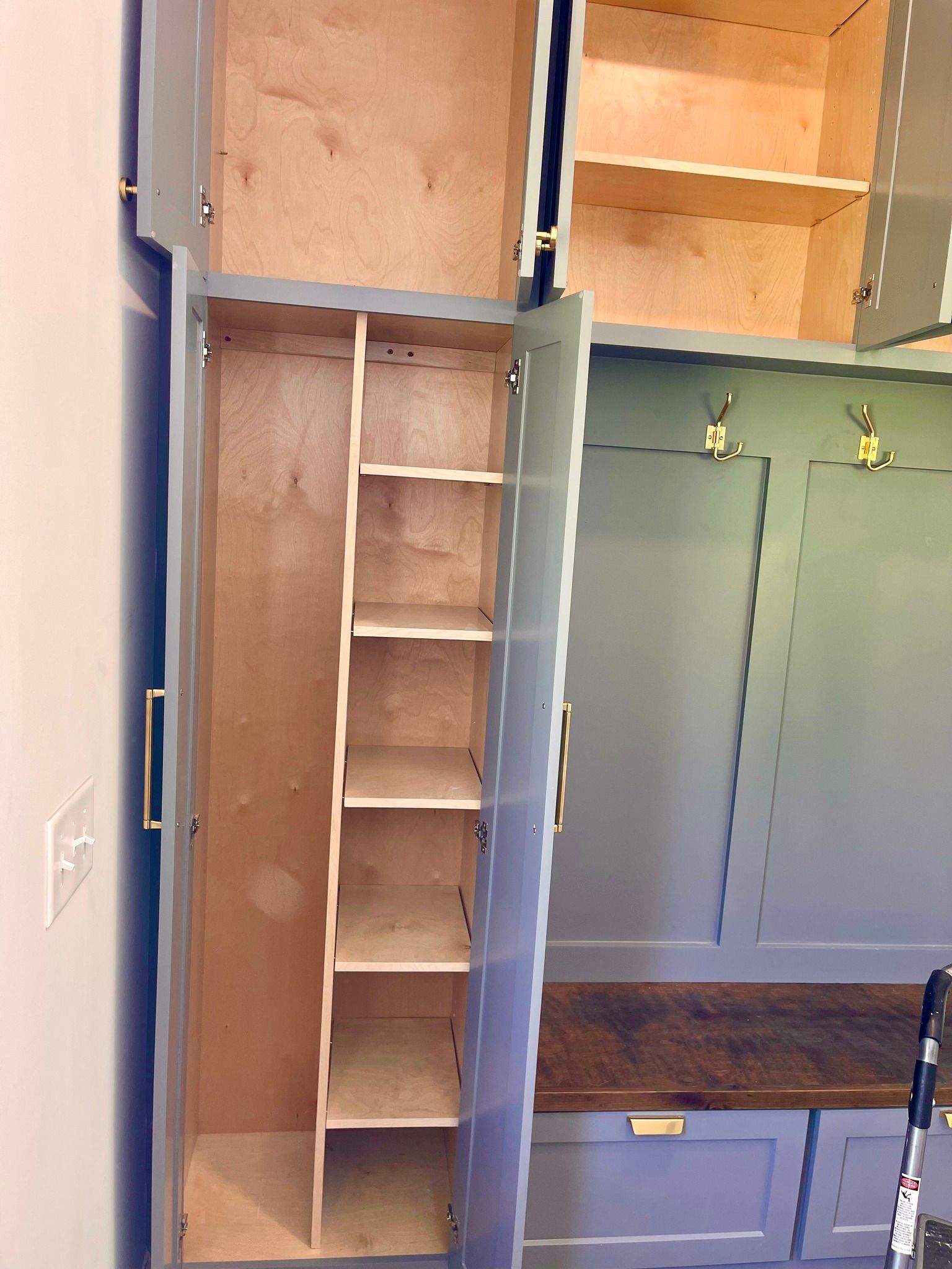 Open closet with built-in shelves, hanging rods, and a bench with hooks in a small room.