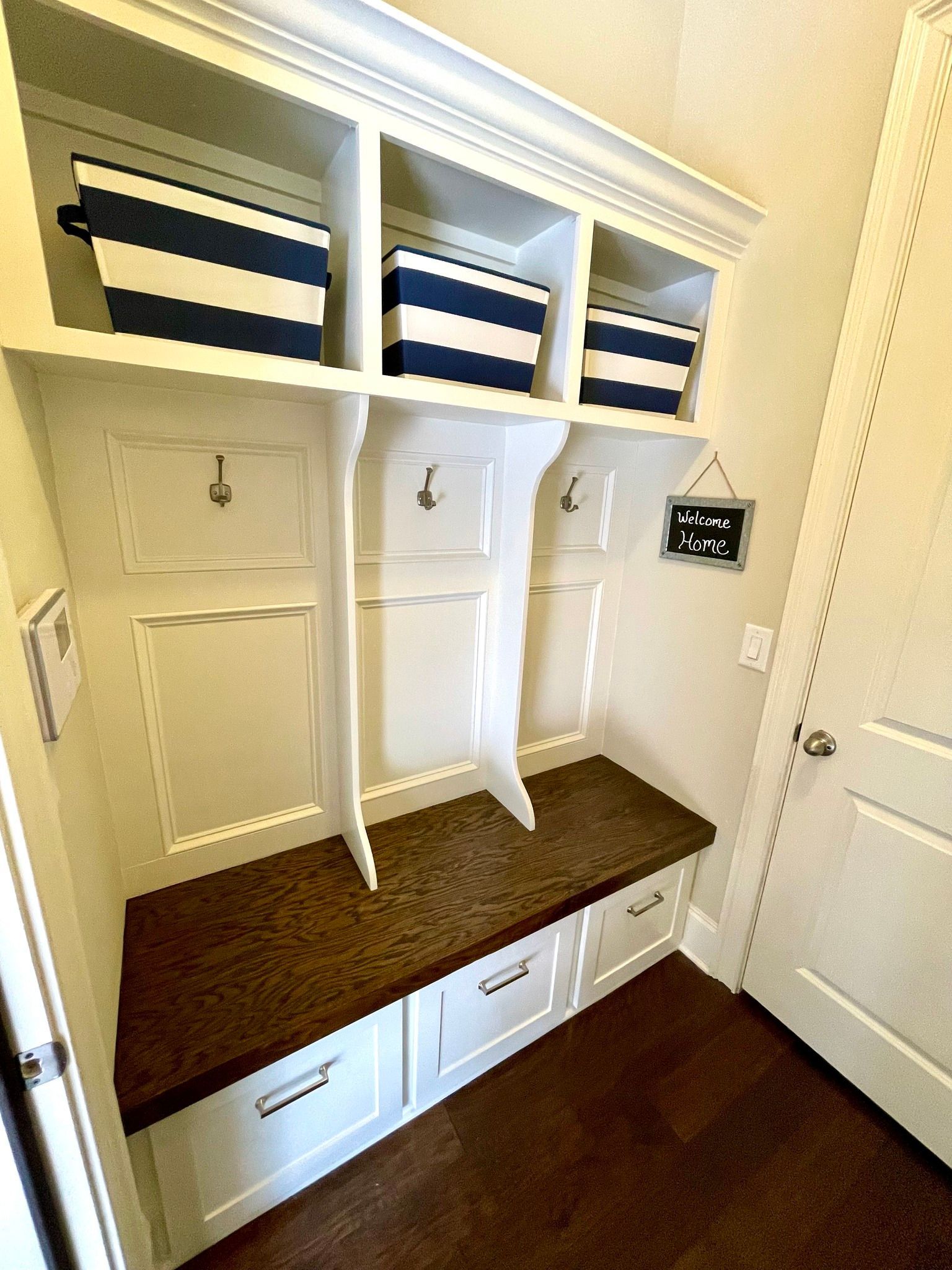 Built-in mudroom bench with cubbies, hooks, baskets, and white storage drawers in a hallway.