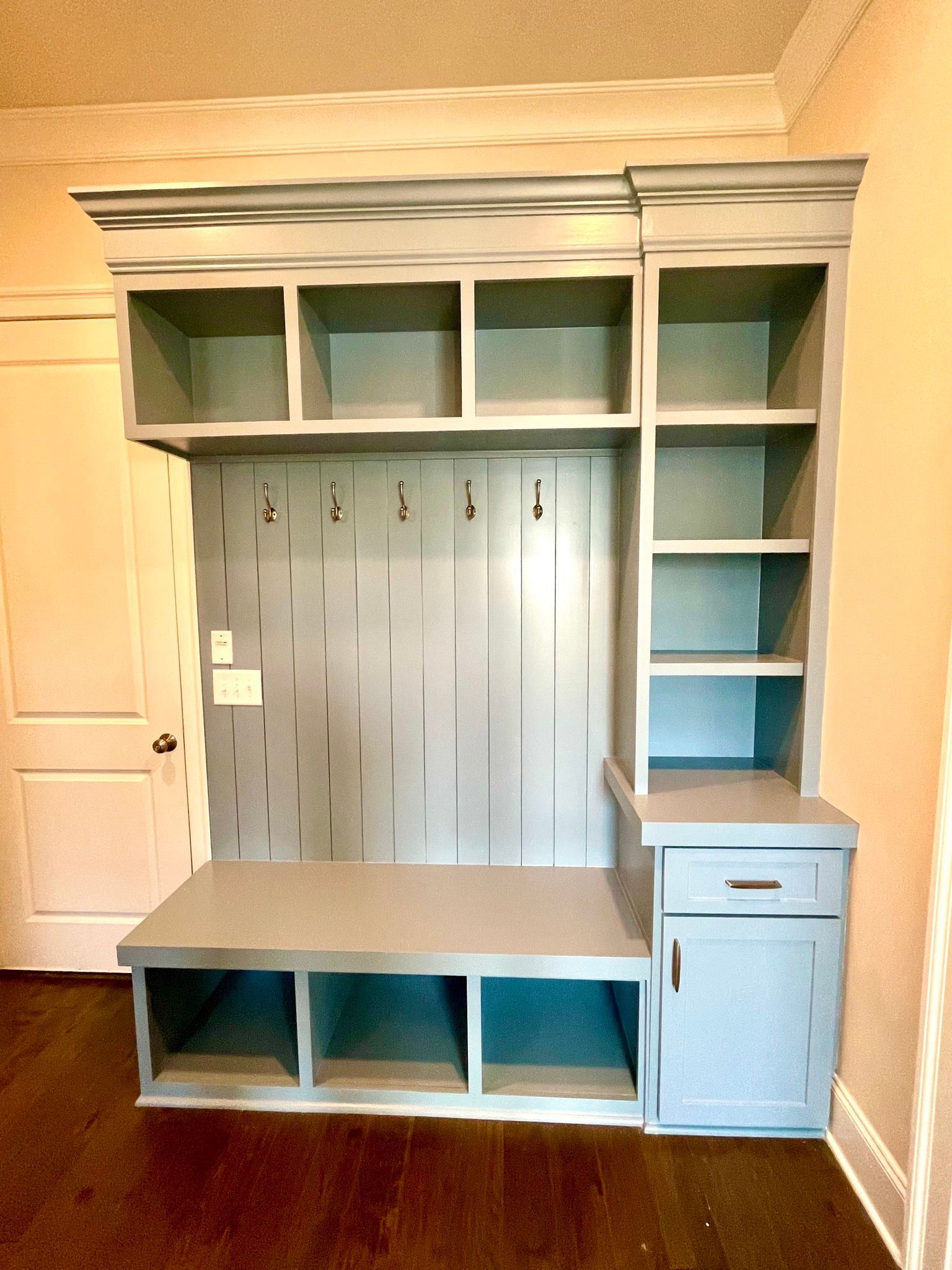 Built-in gray and white storage wall with shelves, bench, hooks, and cabinet in a room