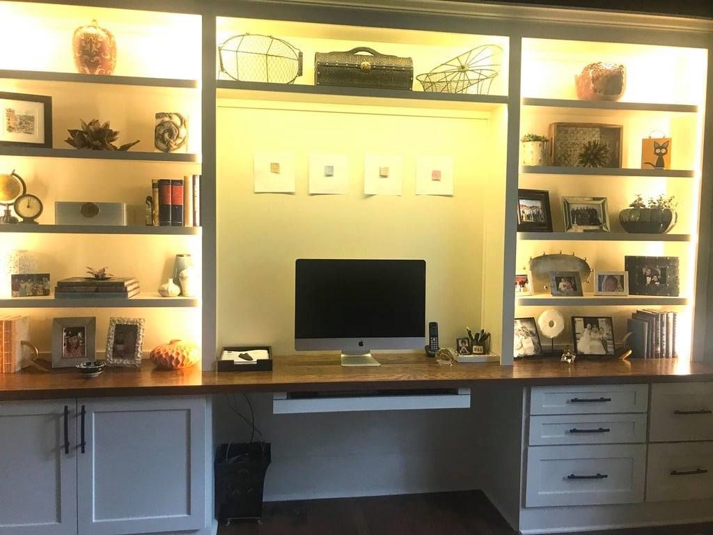 Built-in shelves with decor and a desk nook with a monitor, warmly lit in a living room.