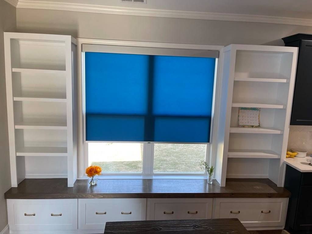 Built-in white cabinets around a window with blue shade and a dark countertop in a bright room