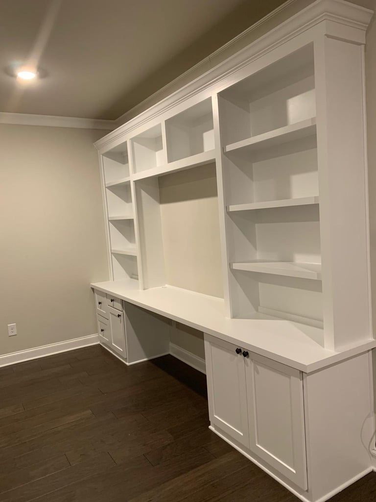 Built-in white shelving and cabinets in a room with dark wood floors and beige walls