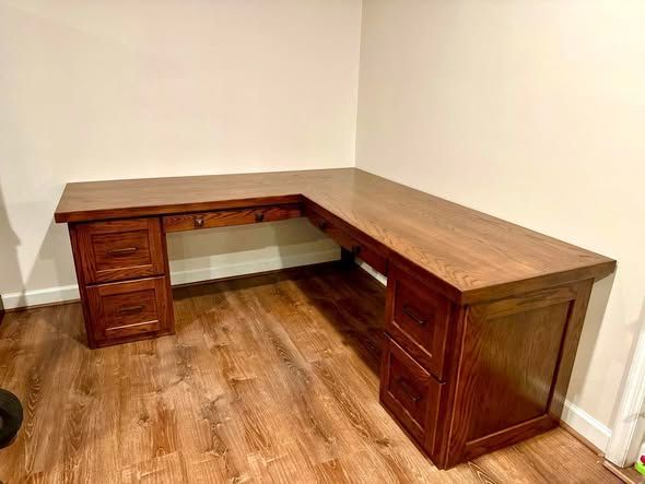 L-shaped wooden desk with drawers in a small empty room on hardwood flooring