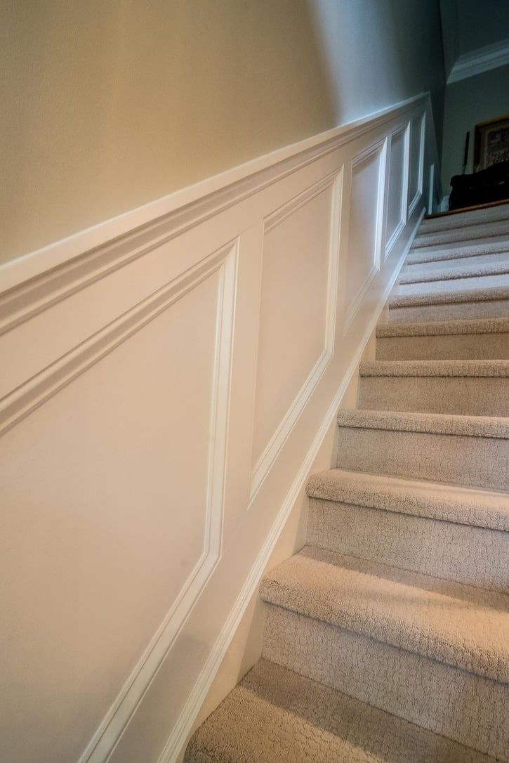 Carpeted staircase with white paneled walls and sunlight streaming down the steps