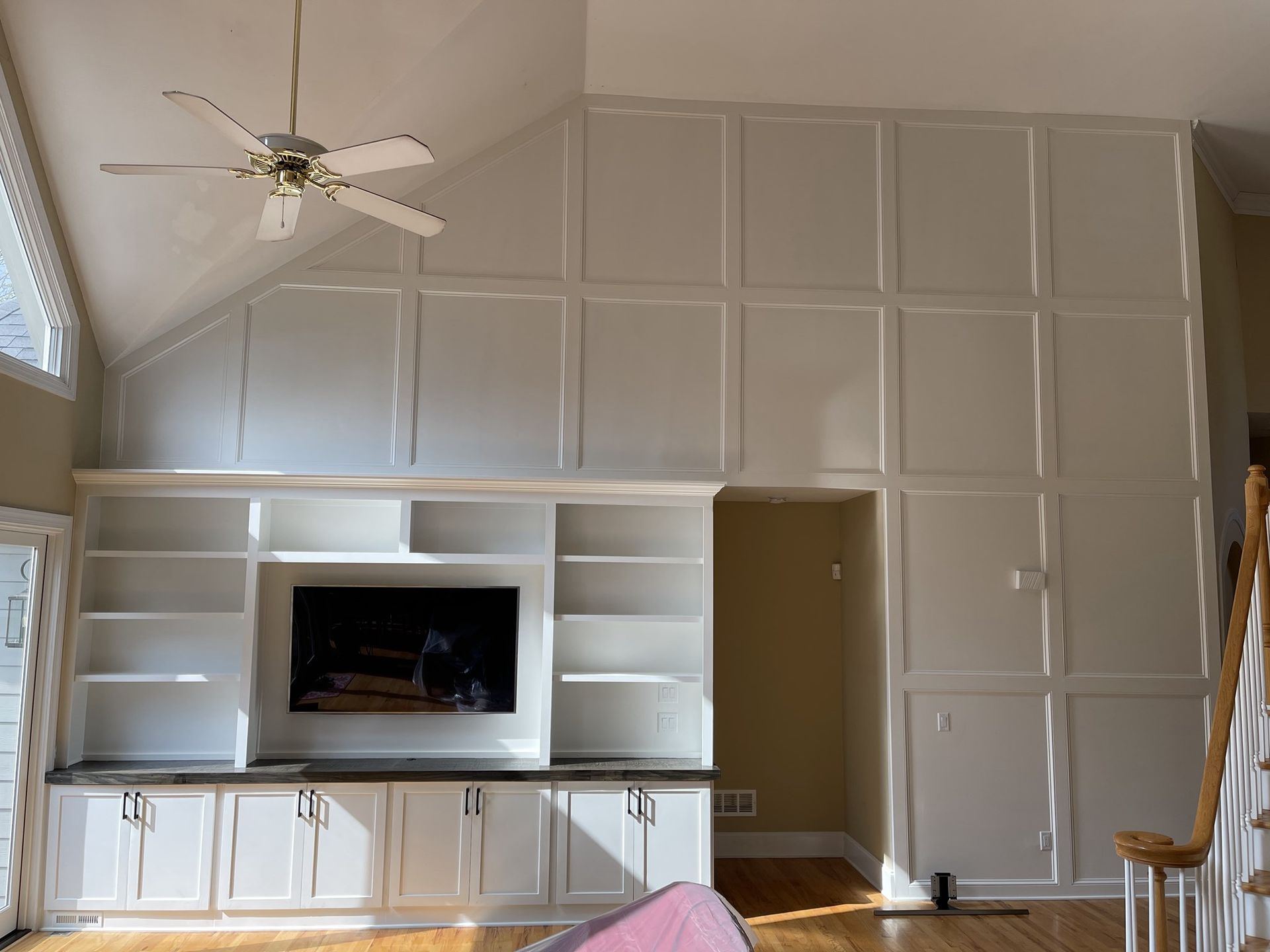 Living room wall of white built-in cabinets with a TV niche, high vaulted ceiling, and ceiling fan