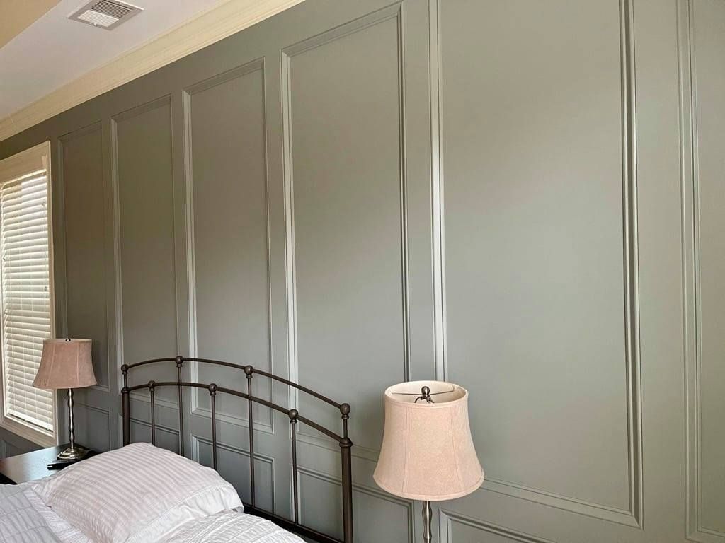 Bedroom wall with gray paneled molding, a black metal bed frame, and two bedside lamps.