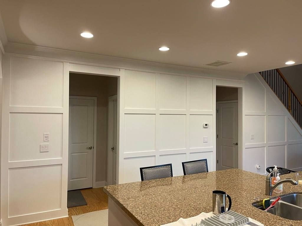 Bright kitchen with white cabinets, granite island, recessed lights, and staircase on the right.