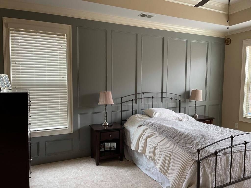 Bedroom with gray paneled walls, a black metal bed, white bedding, and two windows with blinds.