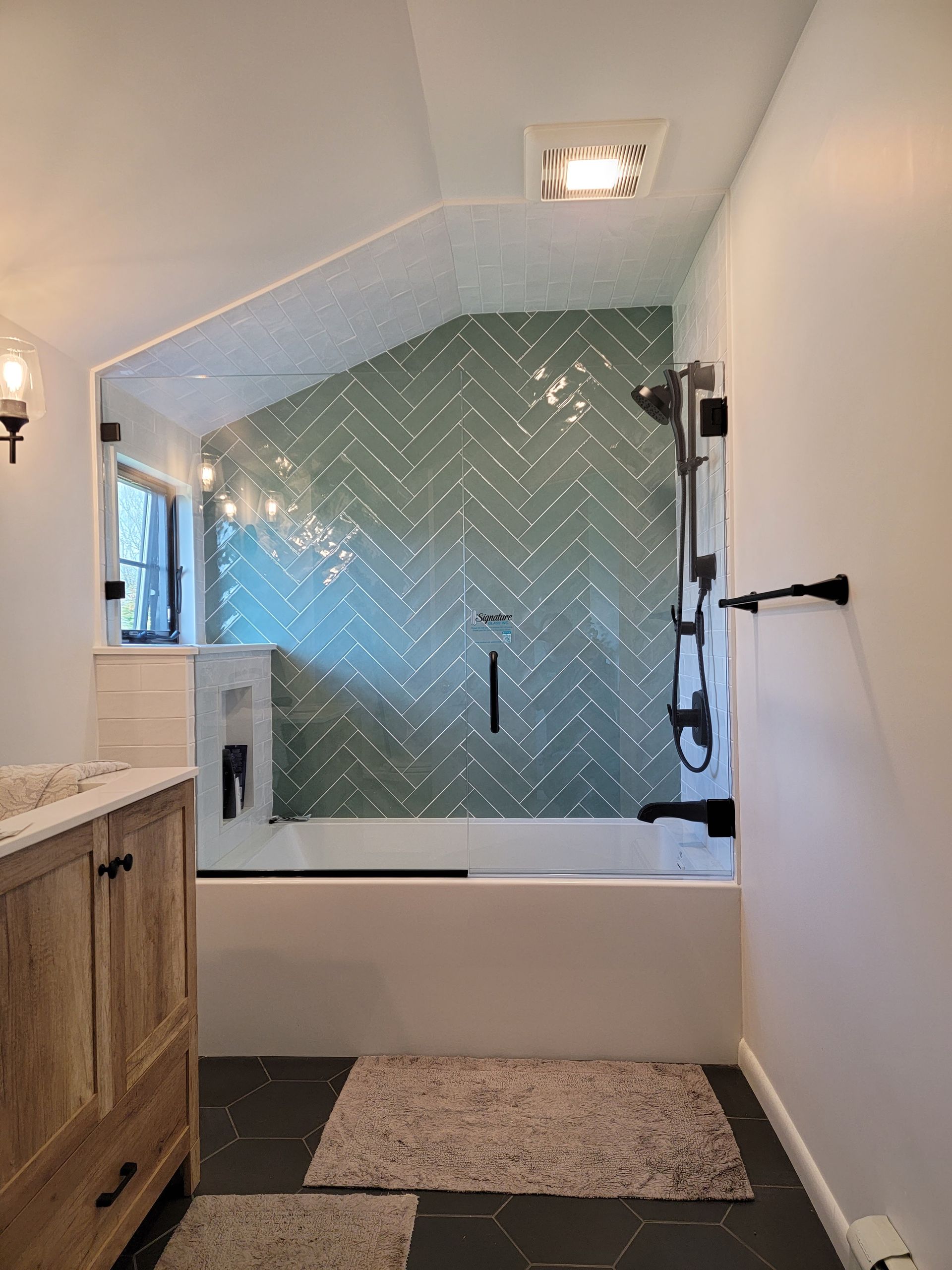 Bathroom with green herringbone tile shower, dark fixtures, and wood vanity.