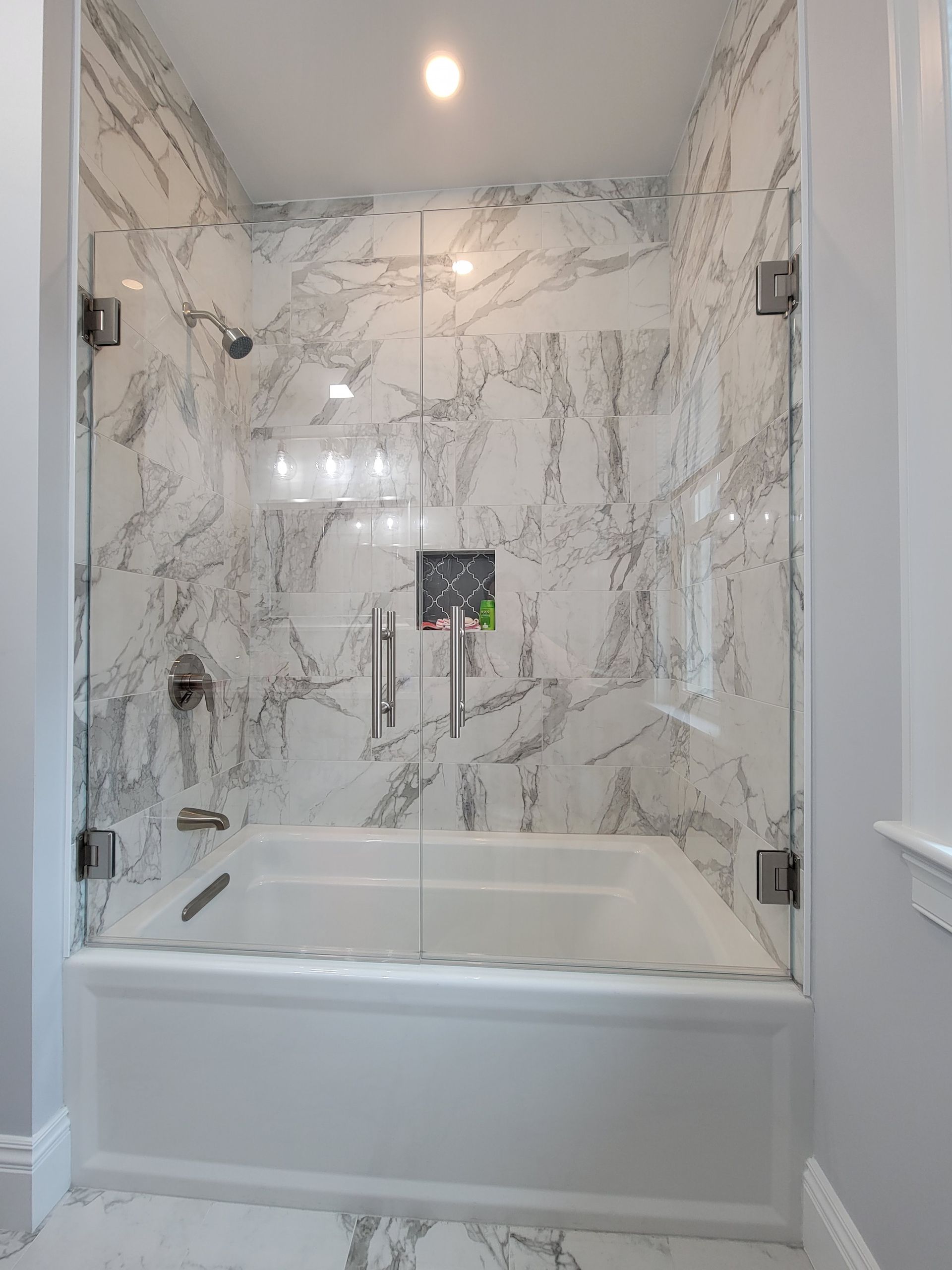 White marble-tiled bathroom with a glass shower door over a white bathtub.