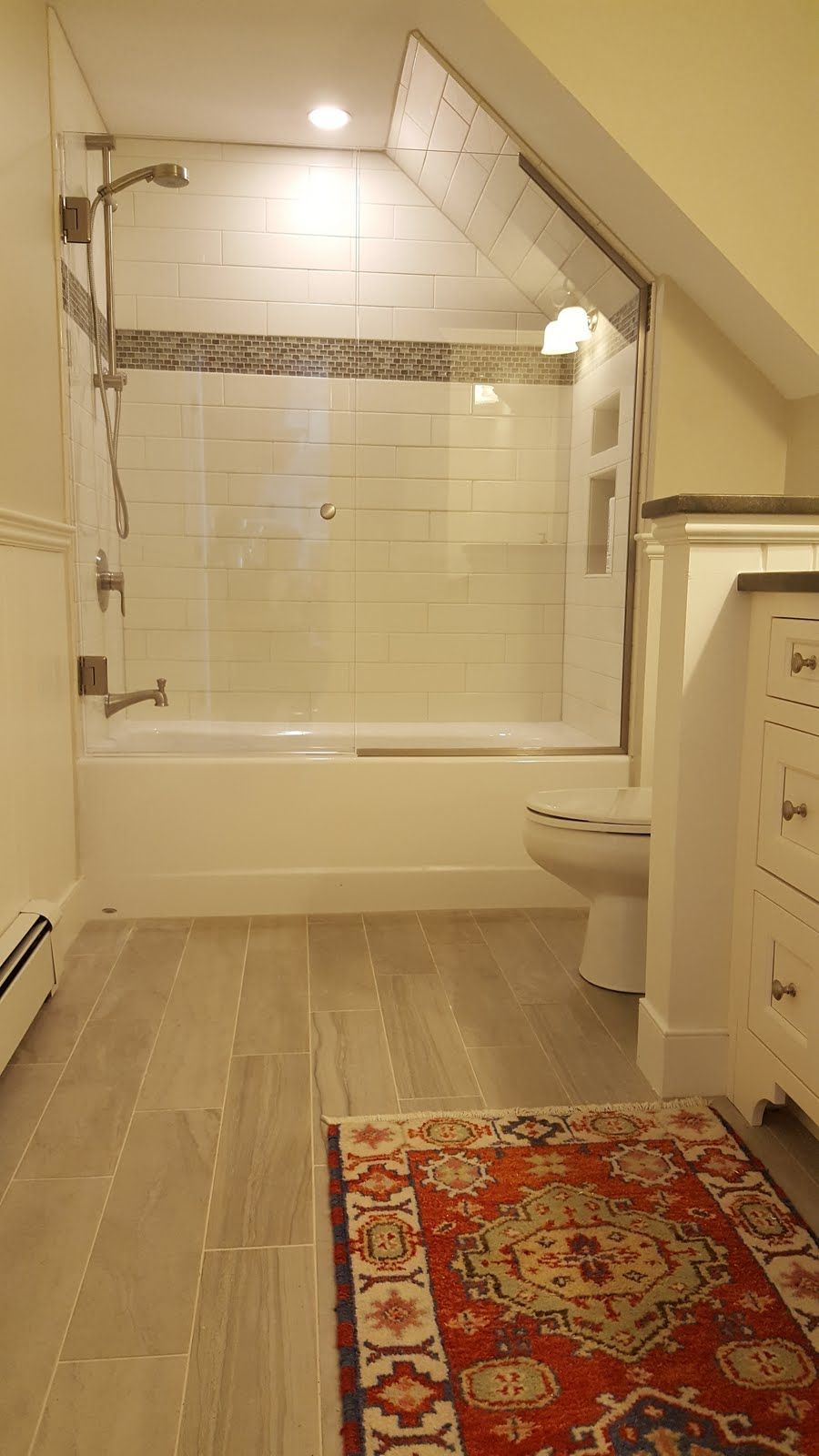 Bathroom with a white tub and shower, tiled walls, and a colorful rug on the floor.