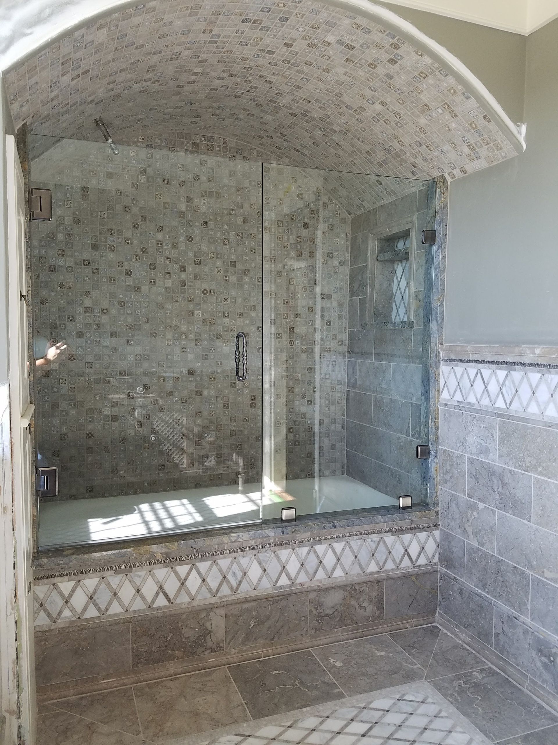 Shower with glass doors and a mosaic tile wall and arched ceiling.