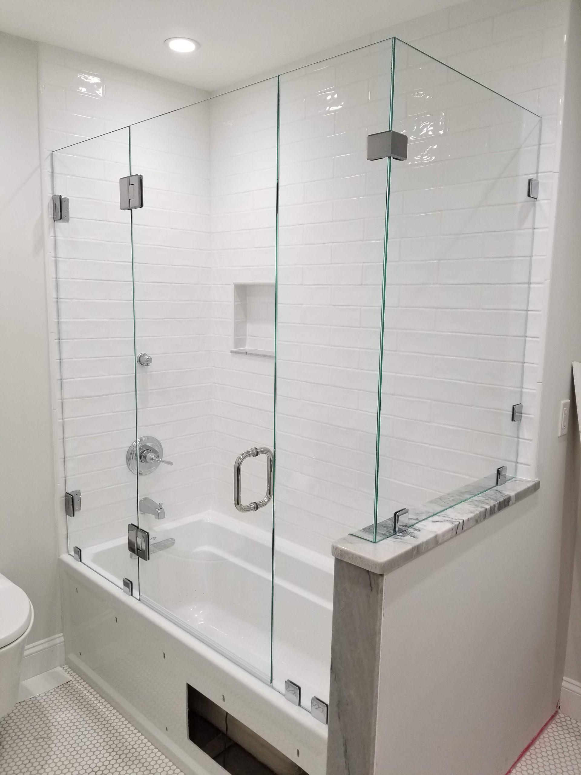 Glass shower enclosure over a white bathtub in a modern bathroom.