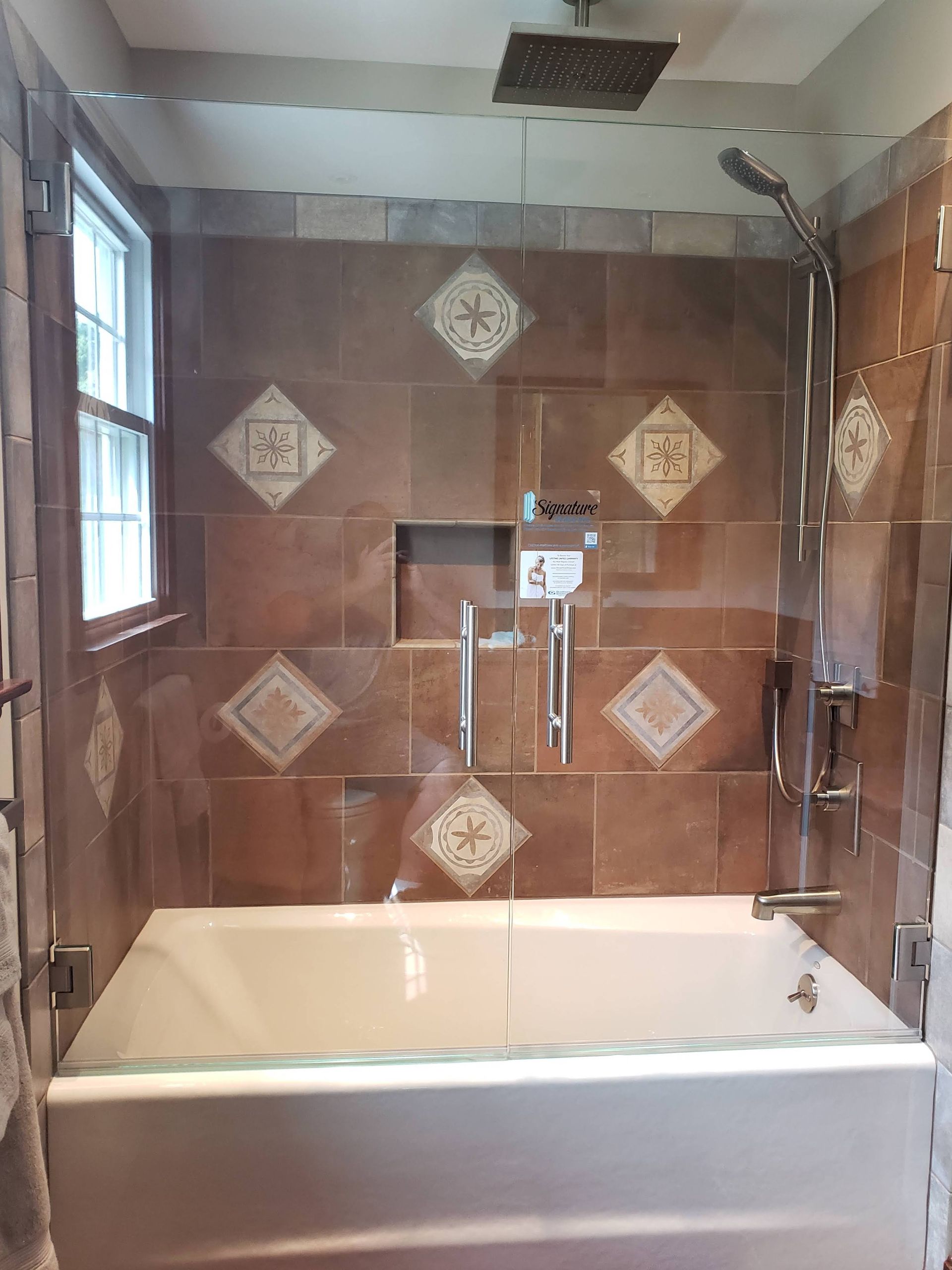 Bathroom with a white bathtub, brown tiles, and a glass shower door.