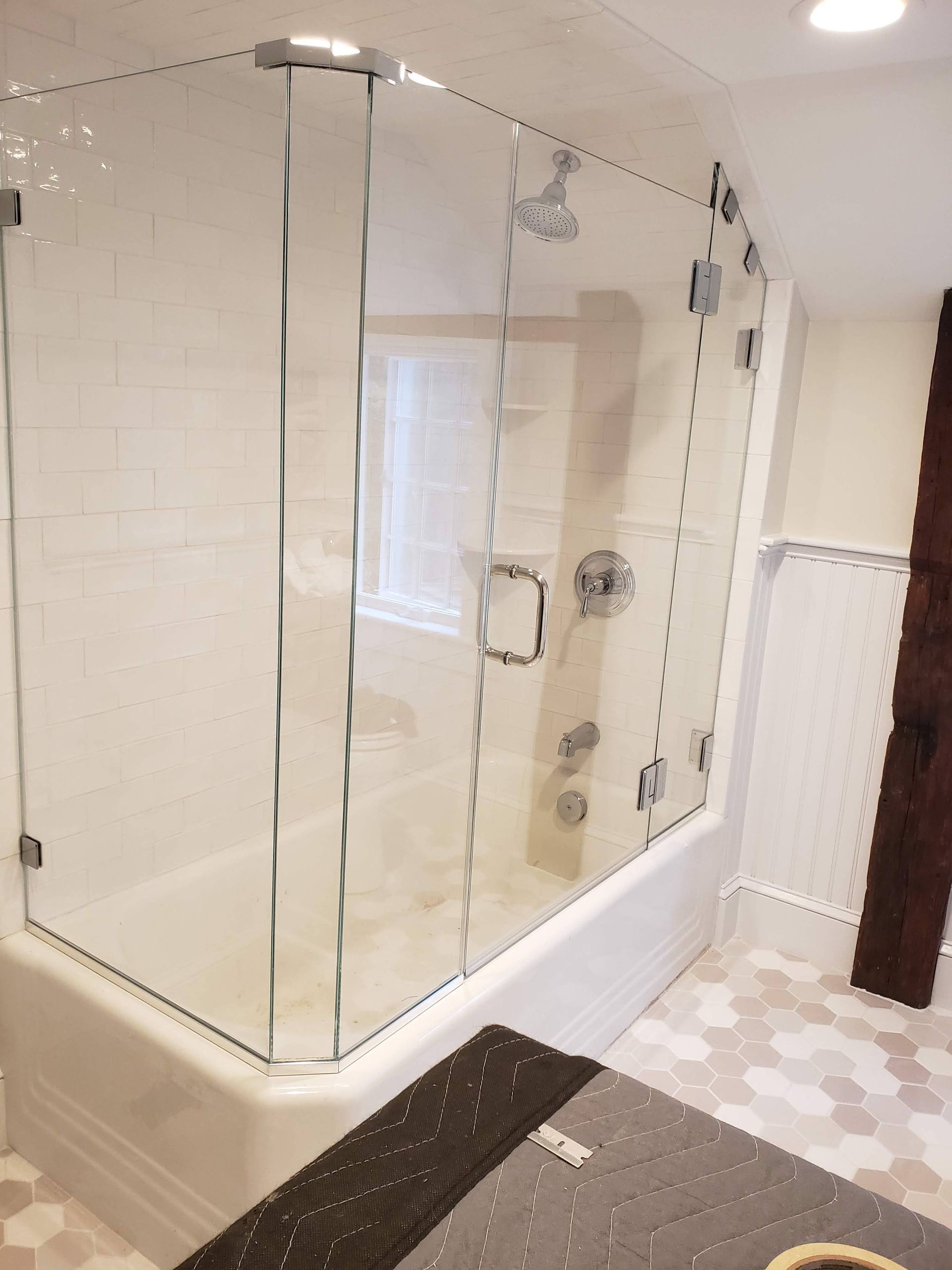 Glass shower enclosure in a bathroom with white tile walls and hexagonal floor tiles.