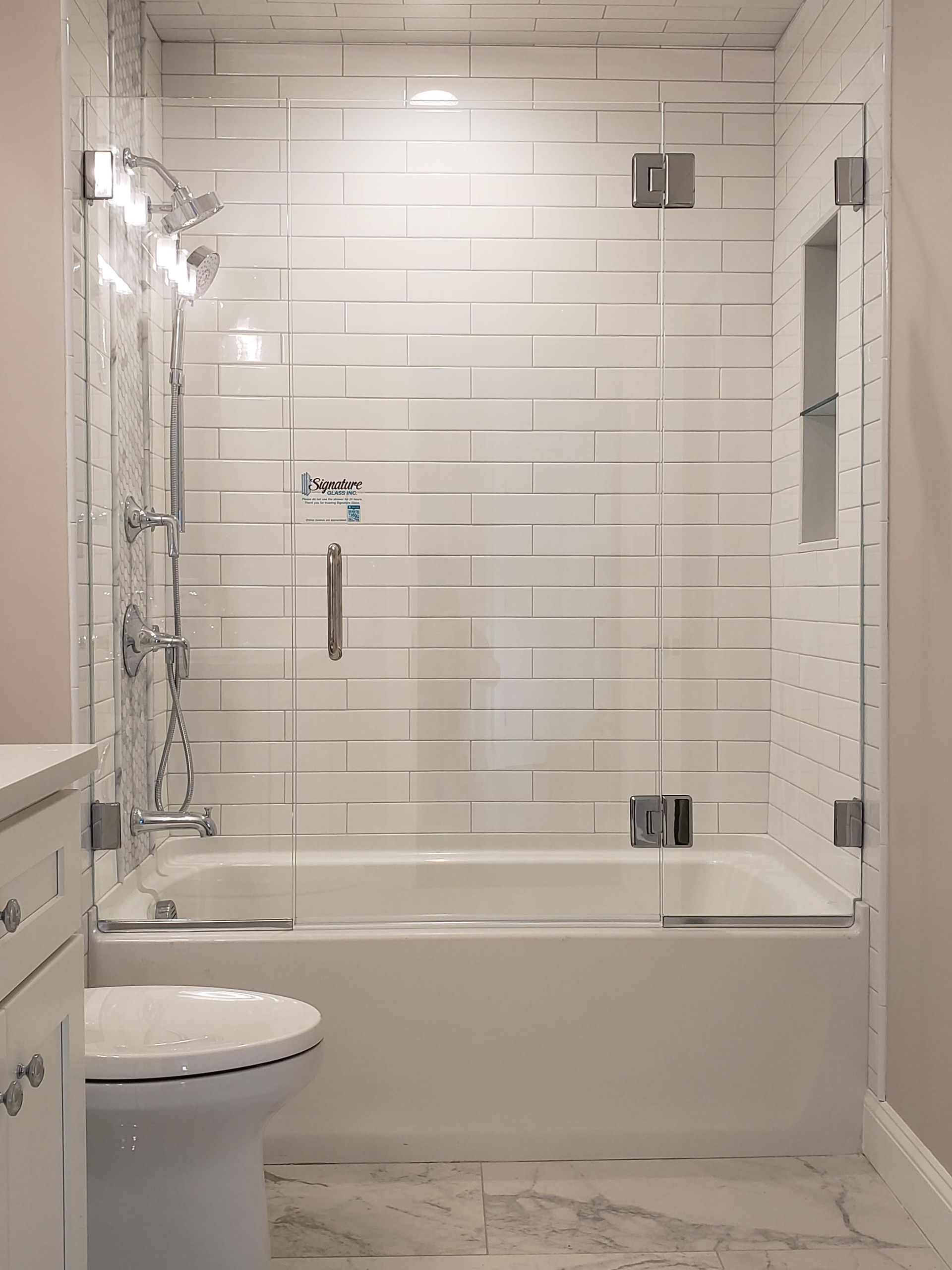 Bathroom with white subway tile, glass shower doors, chrome fixtures, and a white tub.