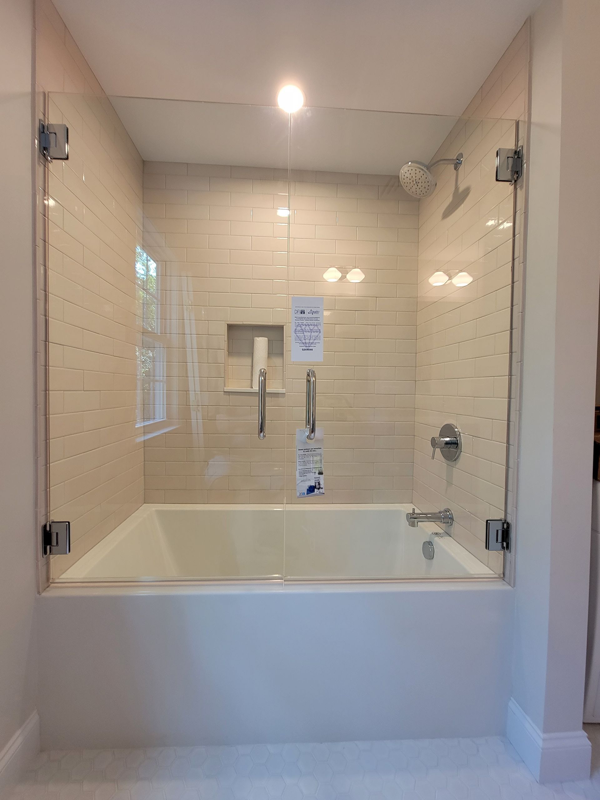 Glass-enclosed shower over a bathtub, with beige tiled walls and a white tub, set in a modern bathroom.