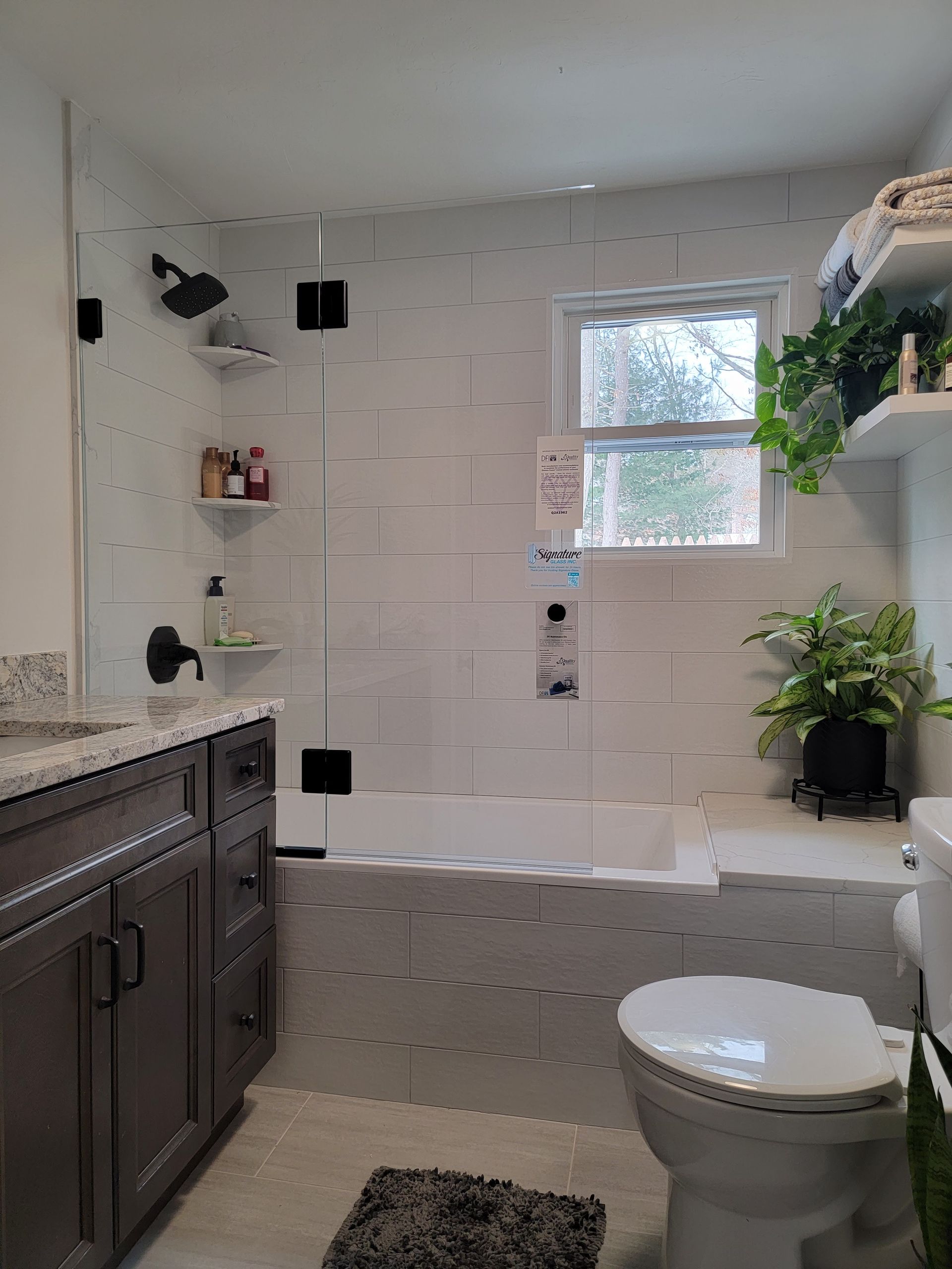 Bathroom with white and gray tile, dark vanity, shower, toilet, and plants.